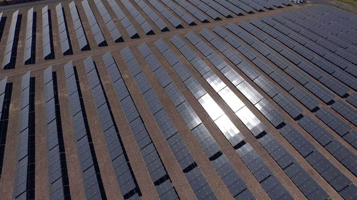 Sunlight reflecting off rows of solar panels in a field aerial