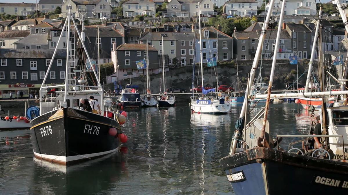 fishing boats moored in harbour with houses in background cornwall uk