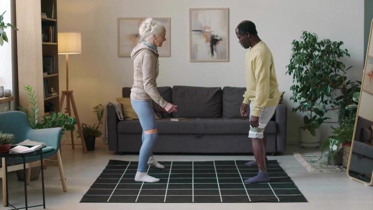 Full side view shot of diverse old couple doing side step squats with resistance bands on their knees while training together at home